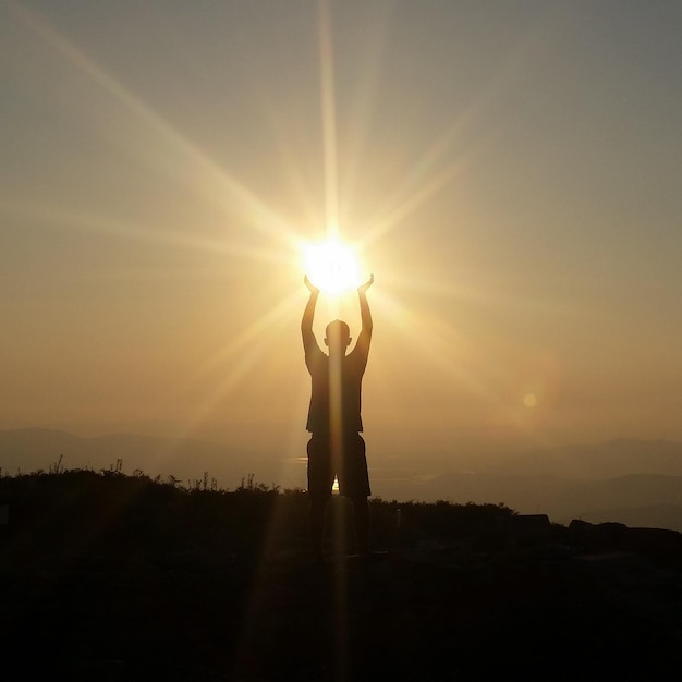 Ilusión óptica de un hombre en silueta sosteniendo el sol contra el cielo durante la puesta del sol