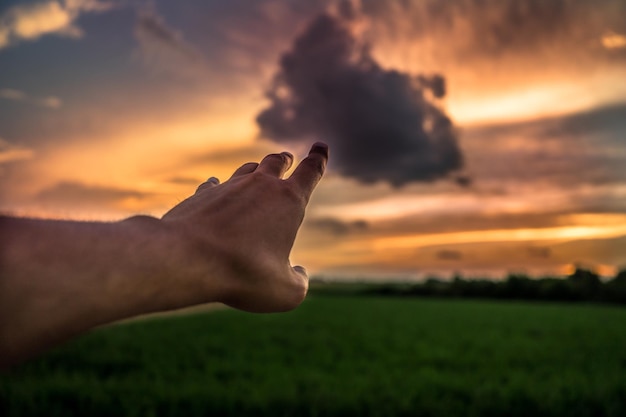 Ilusión óptica de un hombre tocando una nube durante la puesta del sol