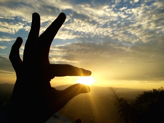 Foto ilusión óptica de la mano sosteniendo el sol contra el cielo por la noche