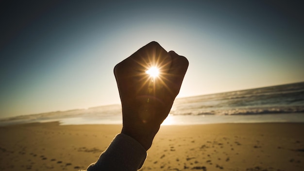 Foto ilusión óptica de la mano sosteniendo el sol en la playa durante la puesta de sol