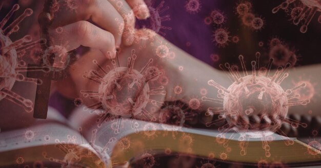 Ilustración digital de células macro Covid-19 flotando sobre manos caucásicas rezando sobre la Biblia con un rosario. Fe religiosa en tiempos del concepto de pandemia global del coronavirus, compuesto digital.