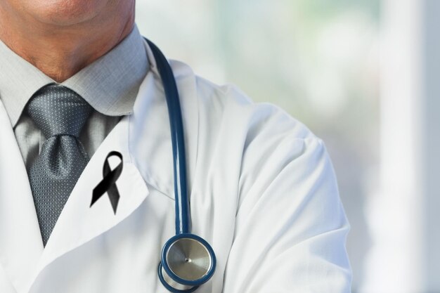 Ilustración digital de un médico caucásico con un alfiler de cinta negra, cruzando los brazos. Compuesto digital de concepto de cáncer de duelo médico