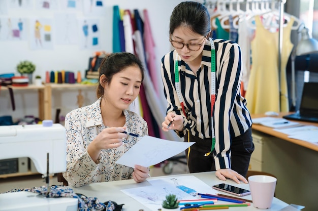 Ilustradores de moda feminina coreana asiática sorridente esboçando e desenhando juntos no atelier moderno. Projeto de discussão de colegas de trabalho criativos de mulheres positivas em estúdio. parceiros que trabalham no local de trabalho.