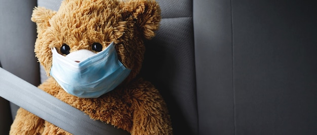 Im Auto sitzt ein brauner Teddybär mit Maske.