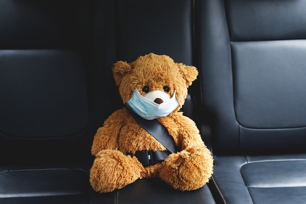 Im Auto sitzt ein brauner Teddybär mit Maske.