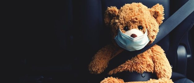 Im Auto sitzt ein brauner Teddybär mit Maske