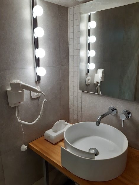 Im Bad gibt es einen Waschtisch, daneben hängt ein Föhn an der Wand, eine Lichterkette an der Wand und ein Spiegel