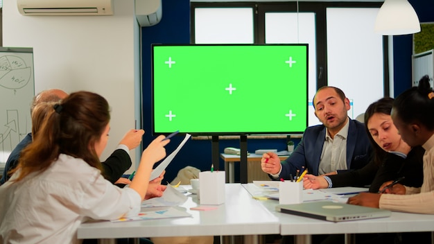 Im Besprechungsraum des Unternehmensbüros steht ein grüner Mock-up-Bildschirm oder ein interaktives digitales Whiteboard im horizontalen Modus. Multiethnische Geschäftsleute arbeiten, Brainstorming im professionellen Start-up