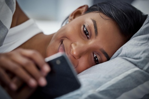 Im Bett in guter Gesellschaft Aufnahme einer schönen jungen Frau, die ihr Handy benutzt, während sie in ihrem Bett liegt