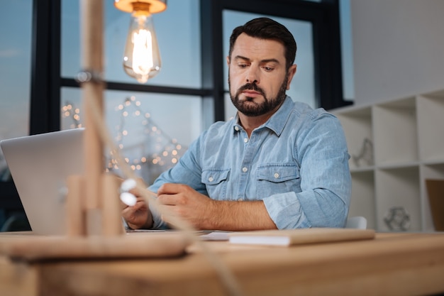 Im Büro. Hübscher kluger hart arbeitender Geschäftsmann, der am Tisch sitzt und seinen Job macht, während er spät abends arbeitet