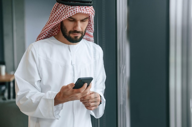 Im Büro mit Telefon Erfolgreicher muslimischer Geschäftsmann in traditioneller Kleidung