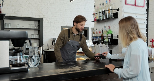 Im Café macht ein Mann Kaffee zum Mitnehmen für einen Kunden, der mit Kreditkarte bezahlt