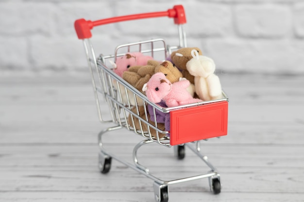 Foto im einkaufswagen liegen viele bunte spielzeug-teddybären. einkaufen auf dem markt. geschenke für geburtstage und feiertage kaufen.