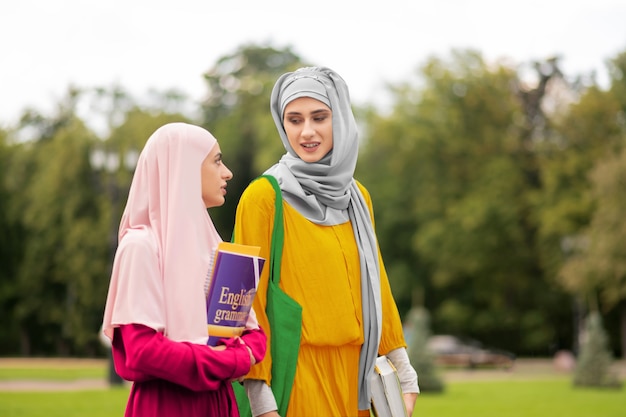 Im Gespräch mit Freund. Muslimischer Student in gelbem Kleid, der mit einem Freund spricht, während er zusammen geht