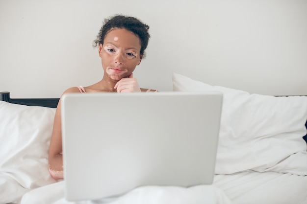 Im Internet. Junge Frau sitzt im Bett und schaut sich etwas auf einem Laptop an