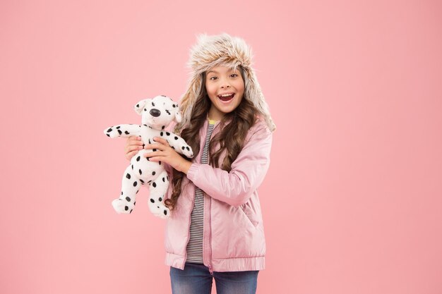 Im Kinderladen glückliches Kind rosa Hintergrund kalte Jahreszeit in warmer Kleidung Zubehör kleines Mädchen Dalmatiner Hund Spielzeug Kind Mode Hipster Mädchen Pelz Winter Ohrenklappe Hut Herbst Stil Kindheitsglück