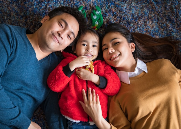 Im Konzept Familienfeier von Dezember bis Januar mit frohen Weihnachten und einem guten Rutsch ins neue Jahr. Asiatische Familie mit Elternteil und Tochter, die lächelt und in die Kamera schaut, fühlt sich glücklich und macht Spaß.