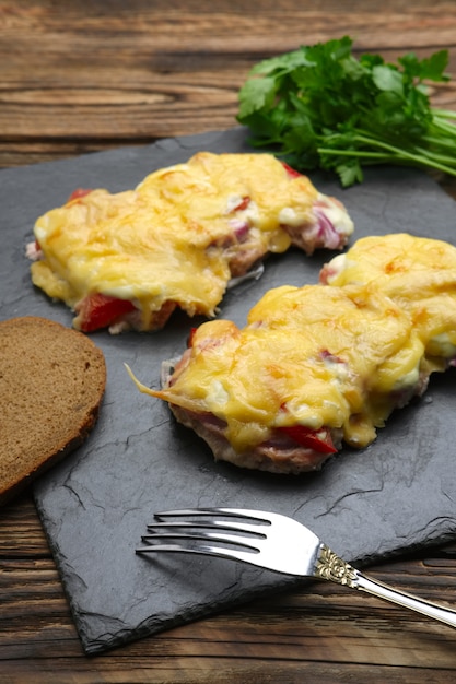 Im Ofen Fleisch mit Champignons, Tomaten und Käse gebacken, Servet auf Steinplatte