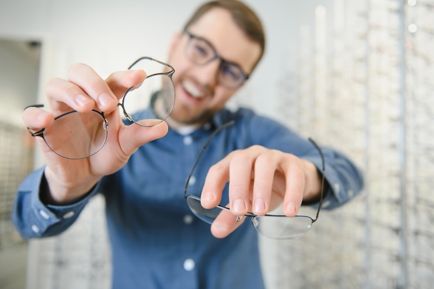 Im Optics Shop Porträt eines männlichen Kunden, der verschiedene Brillen hält und trägt, die im Optikgeschäft eine neue Brille auswählen und anprobieren Mann, der Rahmen für die Sehkorrektur in der Nähe auswählt
