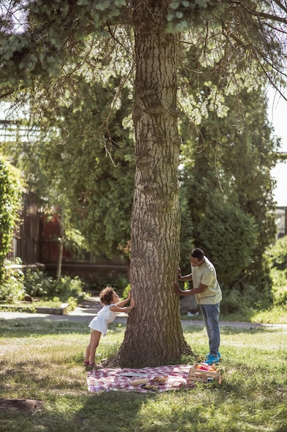 Im Park spielen. Lockiges kleines Mädchen, das mit ihrem Vater nahe dem Baum spielt