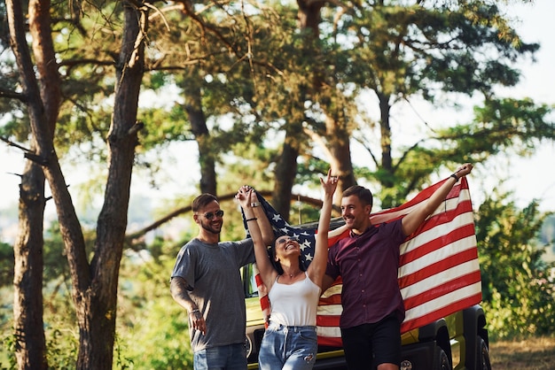 Im Wald. Freunde haben ein schönes Wochenende im Freien in der Nähe ihres grünen Autos mit USA-Flagge.