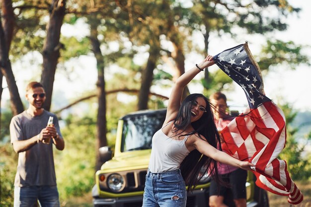 Im Wald. Freunde haben ein schönes Wochenende im Freien in der Nähe ihres grünen Autos mit USA-Flagge.