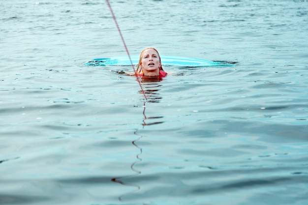 Im Wasser. Schöne blonde kaukasische Frau in einer rosa Schwimmweste, die im Fluss schwimmt, während sie sich an einem Abschleppseil festhält