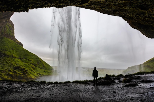 Foto imagem 4k de uma alpinista admirando a cachoeira seljalandsfoss de dentro de uma caverna