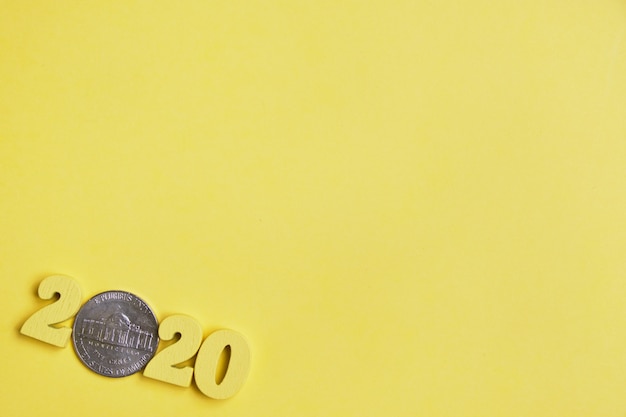 Imagem abstrata de 2020 de figuras de madeira e moedas de centavos em um fundo amarelo. Vista do topo. Copie o espaço.