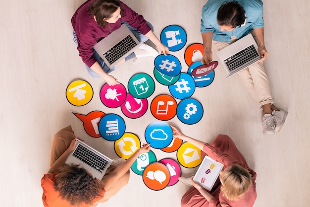 Foto imagem acima de jovens profissionais de marketing de mídia social sentados no chão e usando computadores enquanto analisam ferramentas de marketing