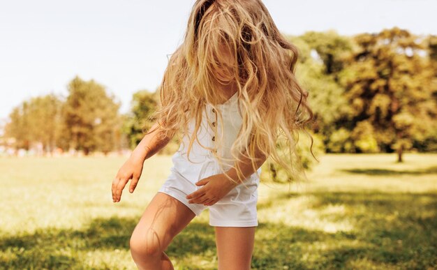 Imagem ao ar livre de sorridente menina adorável com longos cabelos loiros brincando no fundo da natureza Criança feliz aproveitando o horário de verão no parque Criança alegre tem atividade na floresta na luz solar