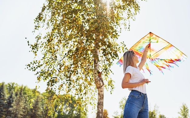 Foto imagem ao ar livre de uma jovem feliz está lançando uma pipa em um dia ensolarado no verão linda fêmea brincando e se divertindo lá fora com uma pipa no parque