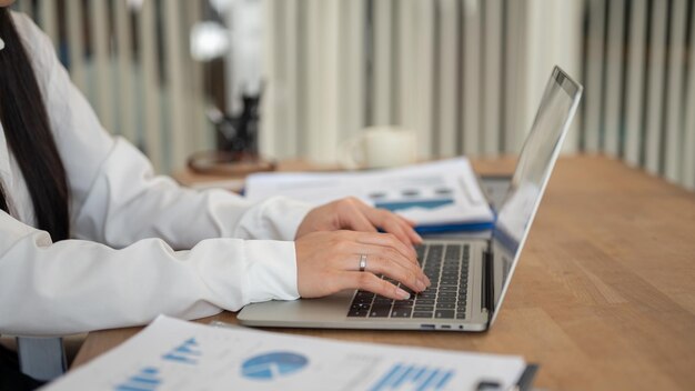 Imagem aproximada da vista lateral de uma empresária trabalhando em seu laptop em sua mesa no escritório