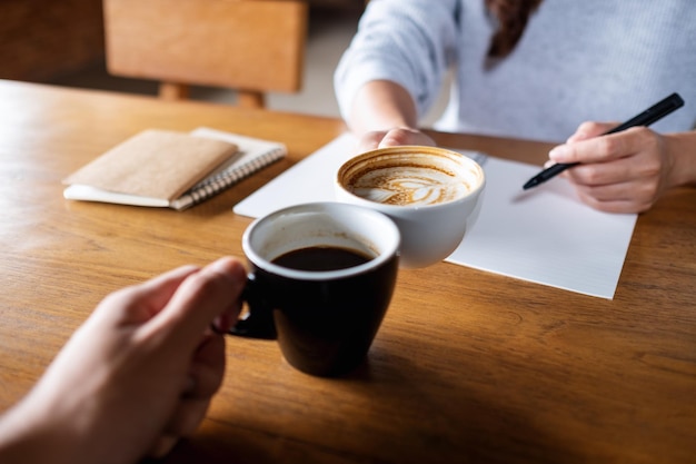 Imagem aproximada de algumas pessoas tilintando xícaras de café enquanto trabalham juntos