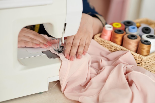 Imagem aproximada de costureira costurando blusa rosa clara de seda para cliente