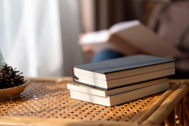 Imagem aproximada de livros na mesa de madeira com turva de uma mulher lendo livro em segundo plano