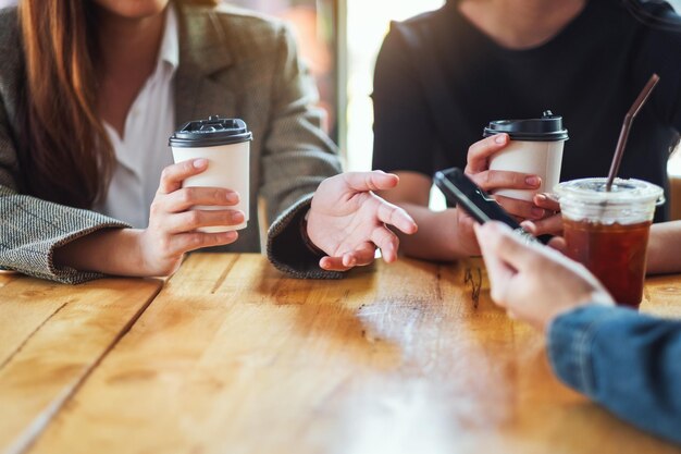 Imagem aproximada de pessoas usando um telefone celular e tomando café juntas