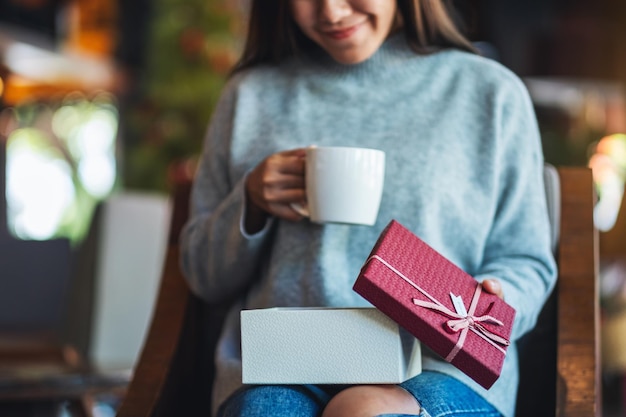 Imagem aproximada de uma bela jovem abrindo uma caixa de presente enquanto bebe café