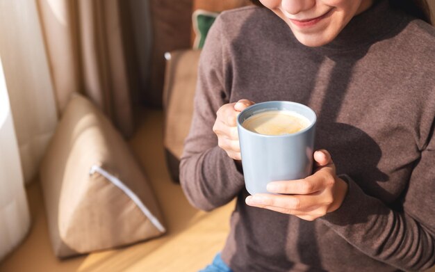 Imagem aproximada de uma bela jovem asiática bebendo café quente em casa pela manhã