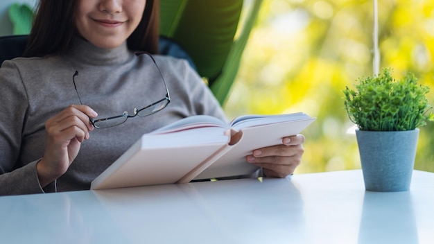Imagem aproximada de uma bela jovem asiática segurando óculos enquanto lê o livro