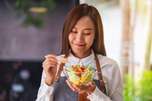 Imagem aproximada de uma bela jovem chef segurando e comendo salada de legumes frescos