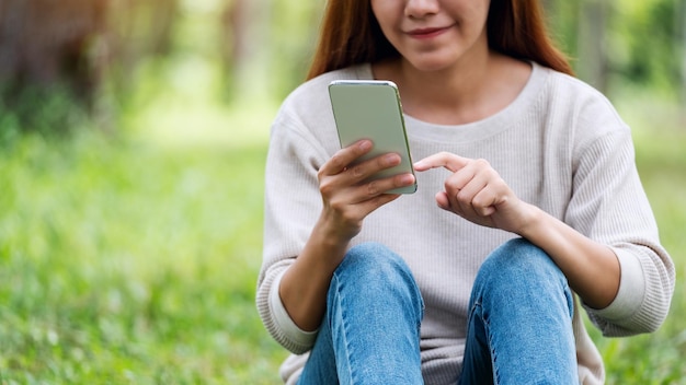 Imagem aproximada de uma bela jovem segurando e usando o celular no parque