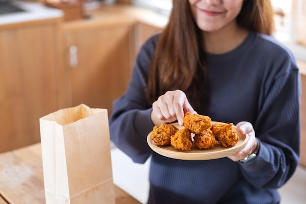 Imagem aproximada de uma jovem asiática segurando e comendo frango frito em casa para o conceito de entrega de comida