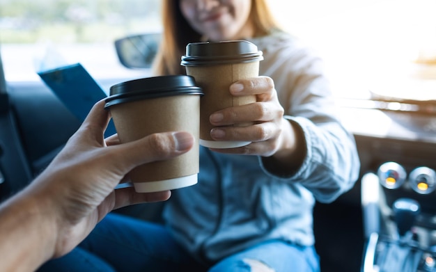 Imagem aproximada de uma jovem tinindo uma xícara de café com um amigo enquanto andava de carro