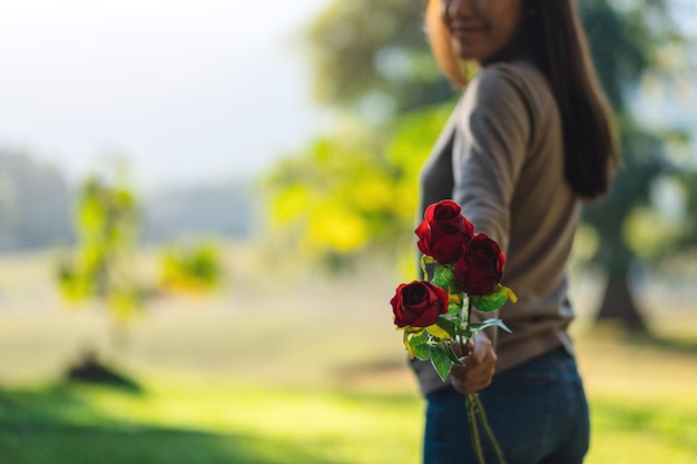 Imagem aproximada de uma linda mulher asiática segurando e dando flores de rosas vermelhas no parque