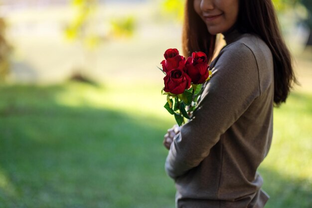 Imagem aproximada de uma linda mulher asiática segurando rosas vermelhas no parque