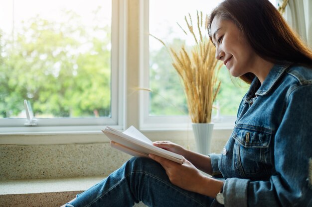 Imagem aproximada de uma linda mulher asiática sentada e lendo livro em casa