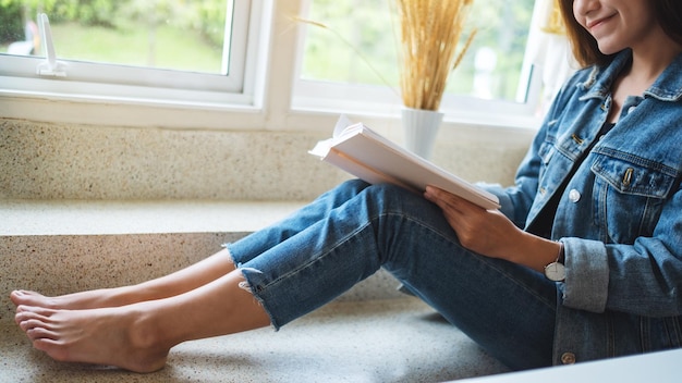 Imagem aproximada de uma linda mulher asiática sentada e lendo livro em casa