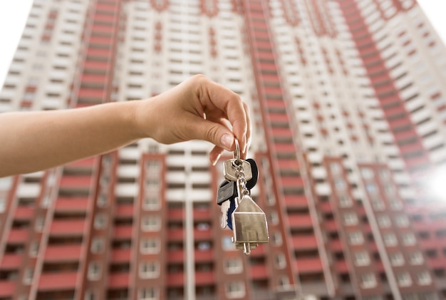Imagem aproximada de uma mão feminina segurando as chaves em um apartamento novo contra um prédio alto