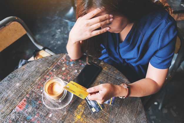 Imagem aproximada de uma mulher asiática estressada e sem dinheiro enquanto segura um cartão de crédito